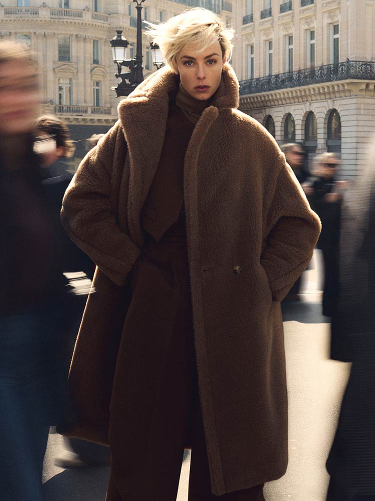Model with Max Mara long Teddy Bear icon coat in camel colour, in a bustling urban environment.